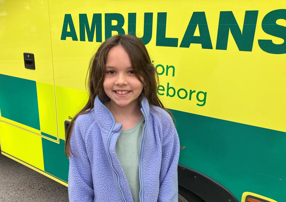 En ung flicka står framför en ambulans.