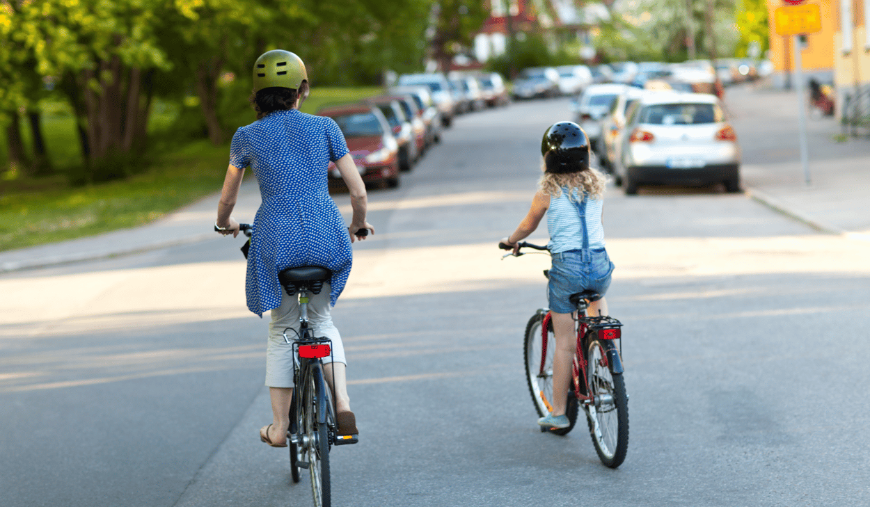 En vuxen och ett barn cyklar längs en gata.