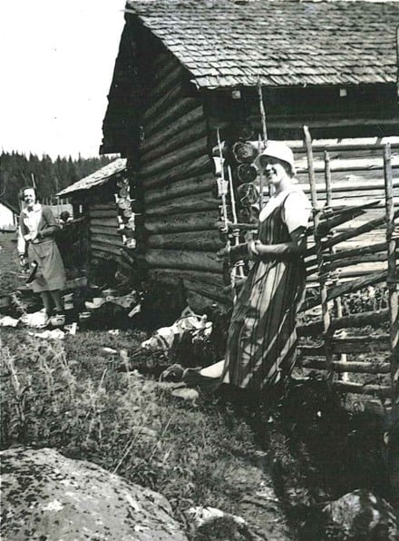 Ett svartvitt foto av en person som st&aring;r framf&ouml;r en stuga.