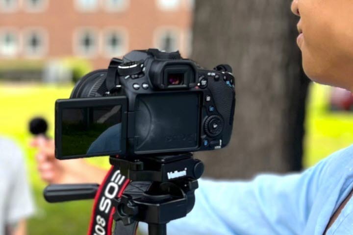 En person framför en filmkamera och en person bakom kameran. 