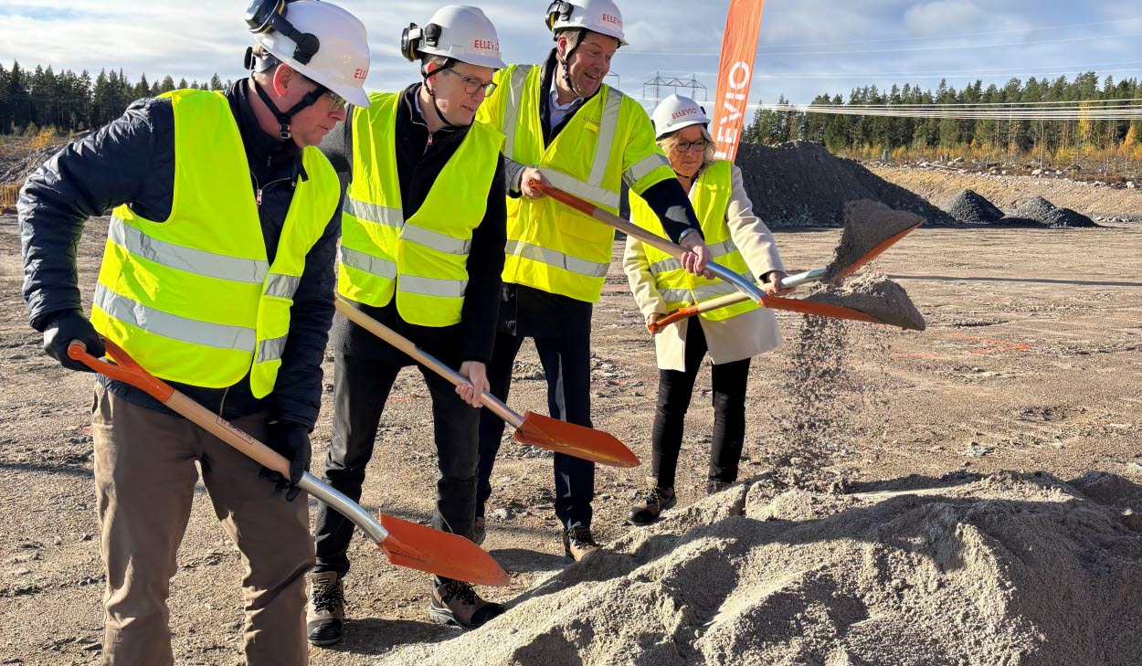 Fyra personer i bygghjälmar och reflexvästar tar första spadtaget med varsin spade på en byggarbetsplats.