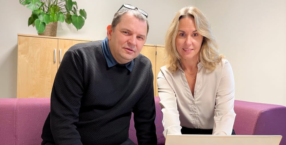 Sam Cole och Malin Schönning sitter i en vinröd soffa med en dator framför sig på ett bord. 
