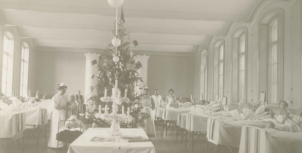 Svart-vit bild med en ny sjukhussal från 1900-talet. Dekorerad med julgran, barn i sängar och vårdpersonal i rummet