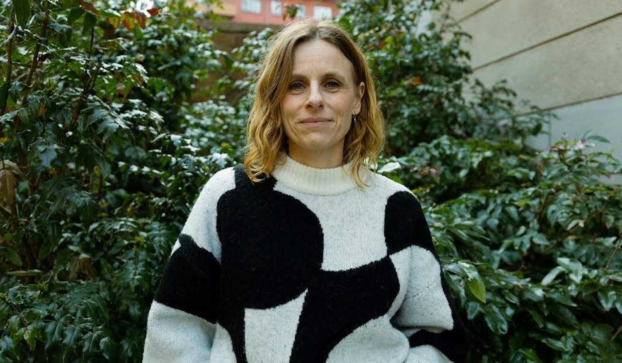 Person ståendes framför en grön buske iklädd en svart och vit mönstrad tröja.